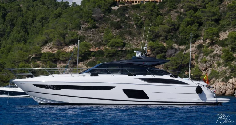 Princess V58 yacht with a white hull and black hardtop anchored beside a wooded cove in Ibiza